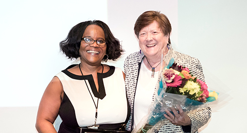 Two people posed together, one with flowers