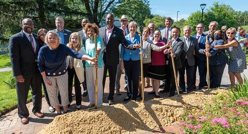 Group of people posing with shovels near a pile of dirt.