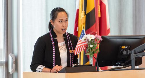 Woman speaking at a podium at the Military Ceremony with the Maryland flag behind her