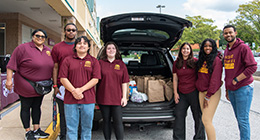 Several HCC students in the Silas Craft Collegians cohort collecting food for a food pantry drive. They are loading several bags of donated food into a van.