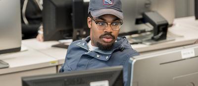 male student sitting behind a desk, facing a computer