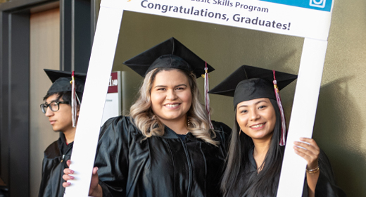 Diploma Recognition two students in caps and gowns holding a large photo frame that says congratulations graduates