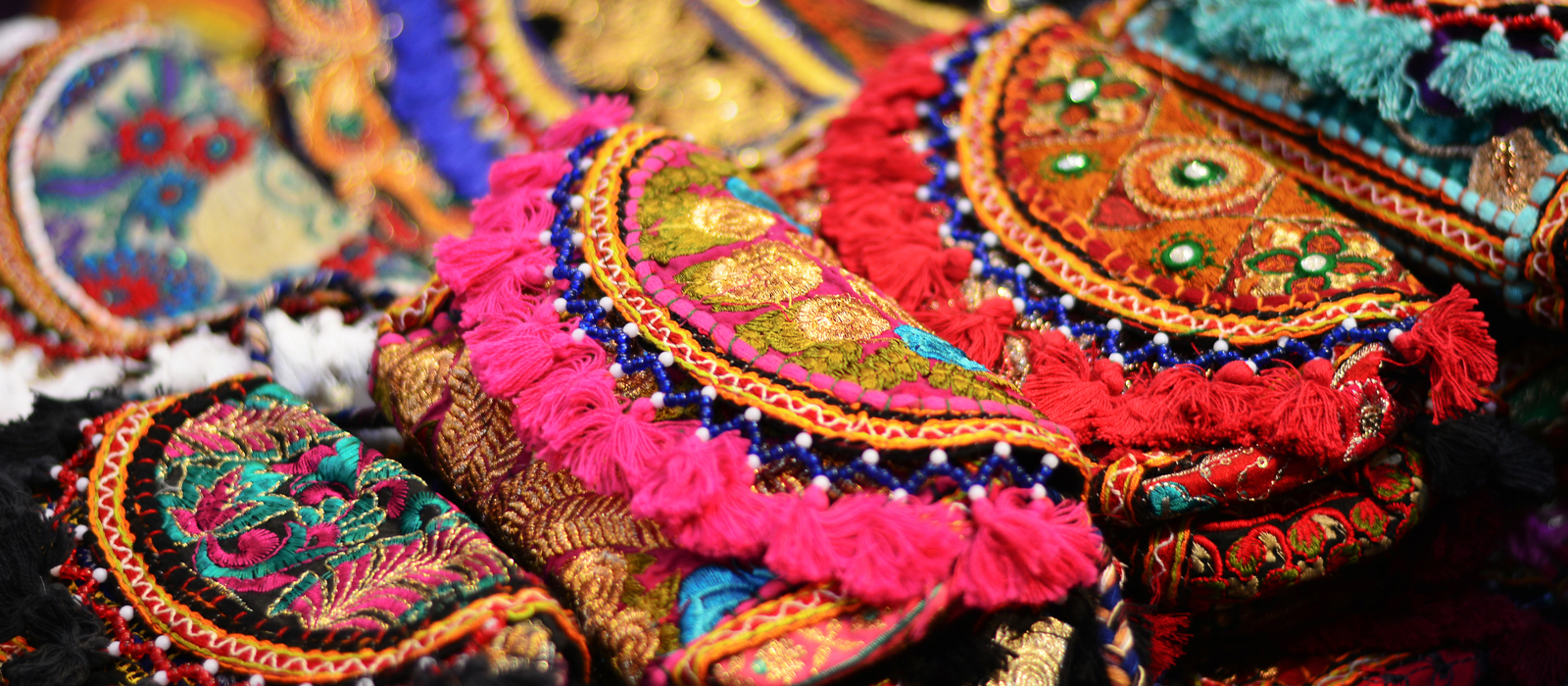 Close-up of colorful handmade Senegalese textiles and embroidered crafts featuring intricate patterns, tassels, and beadwork in vibrant shades of red, gold, pink, turquoise, and green.