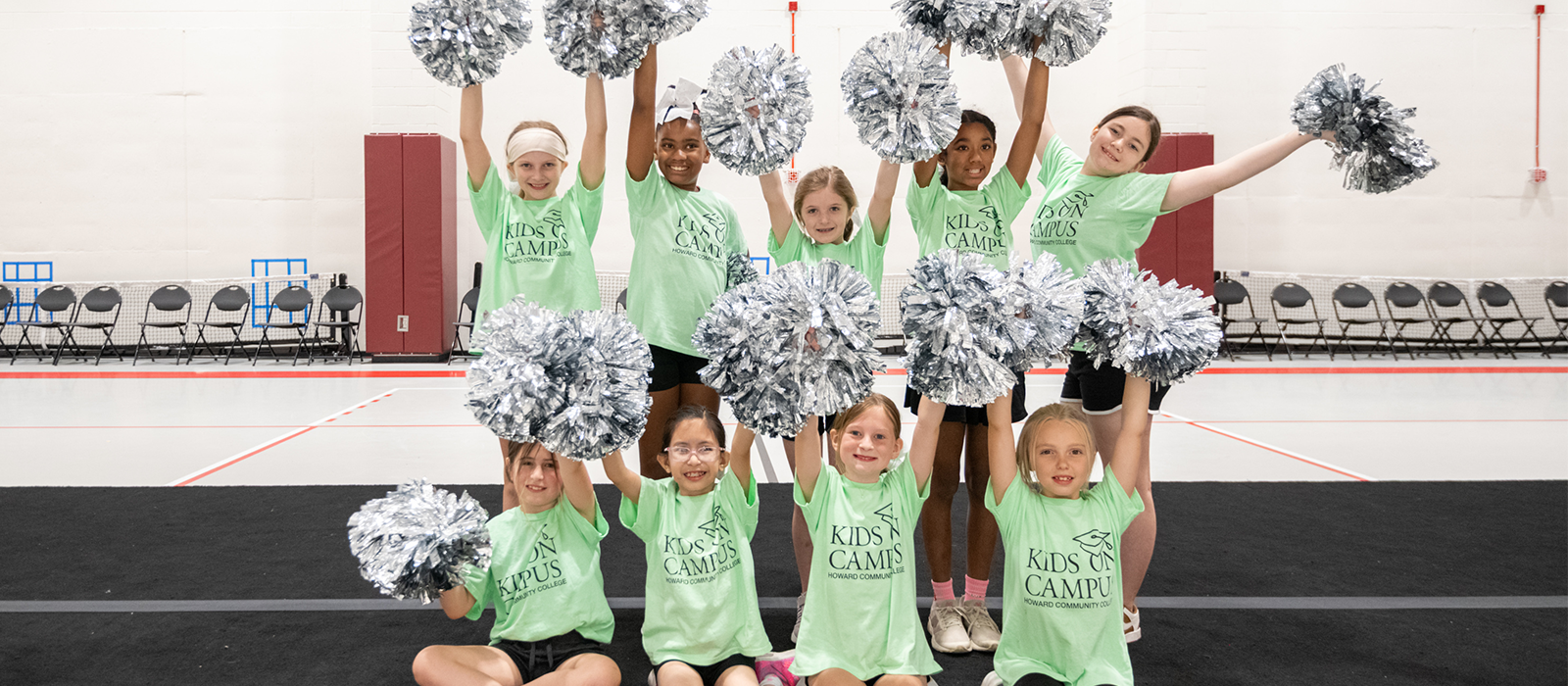 Several young students with a mint green 'Kids on Campus' tshirt pose for a photo in their Cheerleading course.