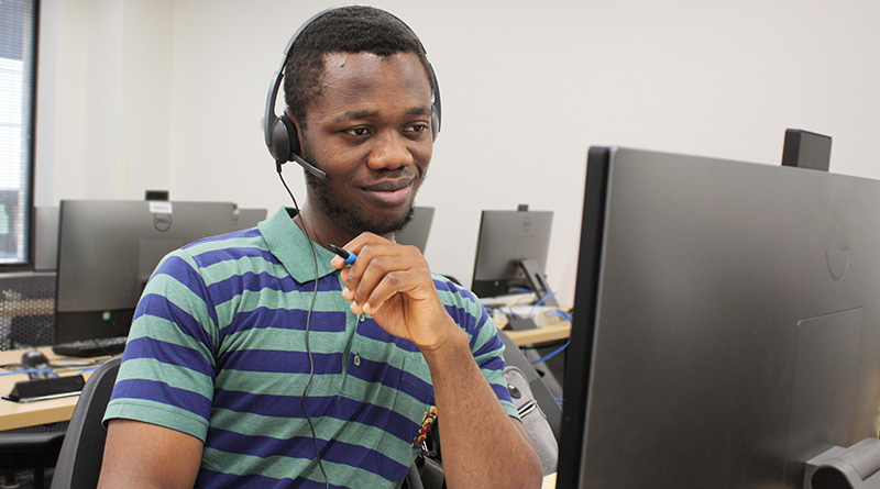 A young black man sits at a computer with headphones on