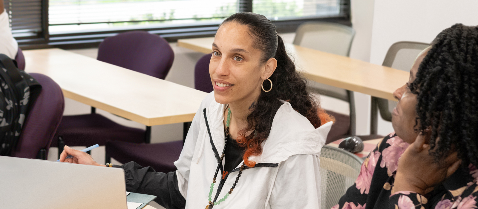 Adult students engaged in a classroom discussion at a community college, with one student speaking while others listen attentively around a table.