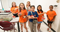 Six children in orange Kids on Campus T-shirts holding small reptiles during an e‑coology class