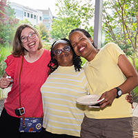 Three women smiling and posing together at a casual event.