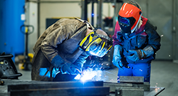 Two students actively welding in a classroom setting.