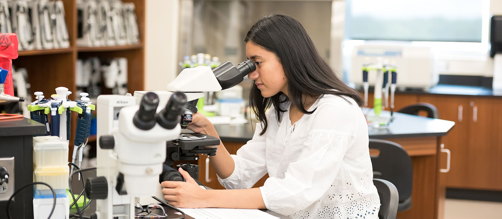 A student sitting at a desk looking into a  microscope
