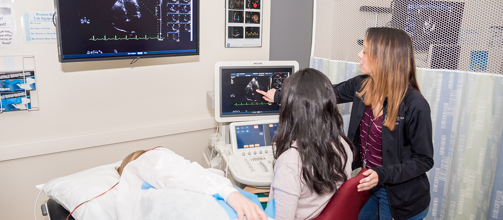 Two people in front of sonography equipment with a patient laying next to them