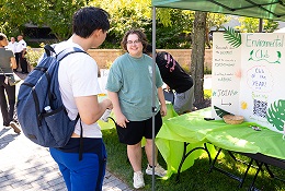 A student speaks with a representative at an Environmental Club booth during an outdoor campus event.